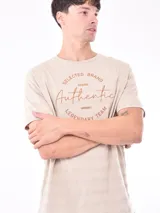 Remera de manga corta color beige con diseño de rayas horizontales sutiles en la textura de la tela y estampado circular en el pecho con la frase 'Selected Brand Authentic Legendary Team'.
