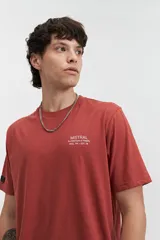 Remera de manga corta color terracota con estampado frontal blanco que dice "MISTRAL Architecture of Reality REG. TM / EST. 76". Tiene un fit regular y está confeccionada en algodón.