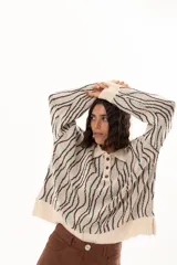 Buzo de tejido de punto con diseño de rayas verticales onduladas en tonos verde y marrón sobre base color crudo. Presenta cuello tipo polo con cierre frontal de botones y mangas largas con puños acanalados.