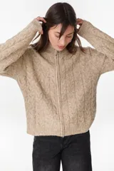 Campera de punto tejido color beige con diseño de ochos, cuello alto y cierre frontal completo.