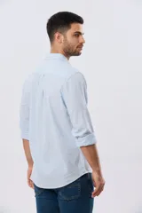 Camisa de manga larga confeccionada en mezcla de lino y algodón, con sutiles rayas celestes, cuello camisero clásico y cierre frontal de botones.