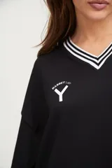 Camiseta negra oversize de manga larga con cuello en V blanco y logo en el pecho.