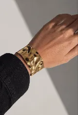 Brazalete rígido de acero quirúrgico con acabado dorado brillante y superficie texturizada con efecto irregular.