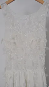 Vestido largo blanco de tul con escote redondo, detalles bordados y apliques en forma de flores.