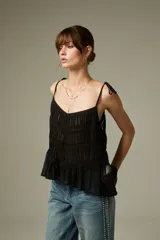Musculosa negra de breteles finos, confeccionada en algodón con diseño plisado y detalles de encaje. Presenta un corte holgado con volados en el ruedo y escote profundo.