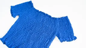 Top de color azul con diseño fruncido en toda la prenda, escote estilo hombros caídos y mangas cortas con terminación de volados.