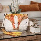 Morral de cuero vacuno color blanco con detalles en amarillo, naranja y marrón. Tiene bolsillo trasero con cierre, cierre superior y tapa con broche. Incluye correa larga ajustable y removible. Interior forrado con bolsillo para celular.
