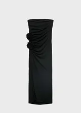 Vestido largo negro de diseño entallado, con escote palabra de honor y sin mangas. Presenta un detalle de flores 3D en la cintura y una apertura lateral en el bajo.