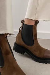 Bota tipo Chelsea de cuero marrón con suela track negra de goma. Presenta paneles elásticos laterales y una costura reforzada en la puntera. Incluye una correa de cuero desmontable con hebilla metálica.
