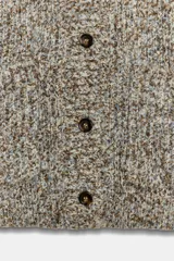 Chaqueta de punto de cuello redondo y manga larga, con textura jaspeada en tonos tierra y azul. Presenta cierre frontal con botones oscuros y dos bolsillos de plastrón en el delantero.