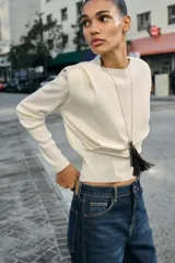 Jersey de punto de cuello redondo y manga larga, con diseño estructurado que incorpora hombreras marcadas y detalles de pliegues en los hombros.