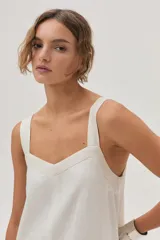 Vestido largo color crema, con breteles anchos y escote recto. Presenta corte irregular en el ruedo y volado en el bajo.