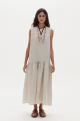 Vestido midi de lino color beige, sin mangas, con cuello redondo y detalles de ondas en las sisas. Presenta un corte con volante fruncido en la parte inferior.