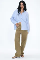 Camisa de manga larga color celeste claro, confeccionada en popelín de algodón. Presenta cuello solapa con botones y un bolsillo de parche en el pecho izquierdo.