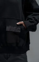Hoodie oversize color negro, confeccionado en frisa gamuzada de algodón. Presenta capucha forrada en microfibra, mangas raglán y un bolsillo frontal tipo canguro con un bolsillo pequeño superpuesto con solapa.