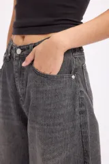 Pantalón de jean estilo baggy, de corte amplio y tiro medio, confeccionado en denim negro con textura de pana fina. Presenta diseño de cinco bolsillos, cierre frontal con botón metálico y cremallera, y perneras holgadas.