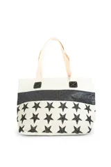 Bolso tipo tote color beige con estampado de estrellas negras, franja superior con brillos negros y asas de hombro en tono crudo.