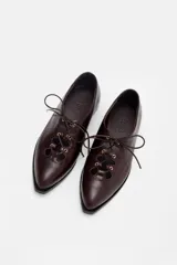 Zapato acordonado de cuero color bordó, con punta fina y diseño estilo oxford. Presenta cordones al tono y detalles de ojales metálicos dorados.