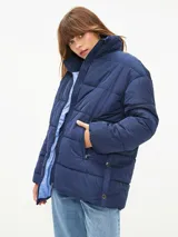 Campera puffer color blanco hueso, con cuello alto, cierre frontal con cremallera y bolsillos laterales con cierre.