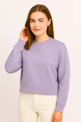 Buzo de cuello redondo en color lila, con detalle de costura en forma de X en el pecho, mangas largas con puños elásticos y corte cropped.