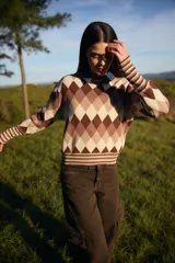 Sweater de punto con diseño de rombos en tonos marrones, beige y crema. Presenta cuello redondo, mangas largas con puños anchos acanalados y diseño de rayas en los puños y el ruedo.