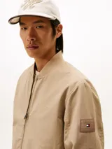 Campera estilo bomber Tommy Hilfiger color beige, con cierre frontal de cremallera, bolsillos laterales de ojal, puños y dobladillo de canalé. Cuenta con el logotipo de la marca bordado en el pecho y un parche distintivo en la manga.