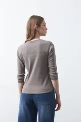 Remera de manga larga color beige, confeccionada en algodón, con escote en V y cartera corta de botones blancos.