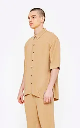 Camisa de corte oversize, color beige, con cuello clásico, cierre frontal de botones y mangas cortas. Confeccionada en tejido de lino.