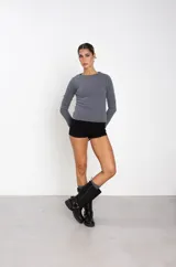 Bota de caña alta estilo biker, confeccionada en cuero sintético negro. Presenta una hebilla ajustable en la parte superior de la caña y un arnés decorativo en el tobillo con argolla metálica y remaches.