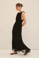 Vestido largo de gasa color negro, con escote profundo adornado con volados, lazos en el cuello con terminaciones metálicas y corte en la cintura con cinturón a tono.