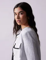 Chaqueta de tweed negra marca Nanette, con escote a la base, abertura central con botones, bolsillos delanteros, aplique de botones perlados en los puños, ribete en contraste blanco y forro interno.