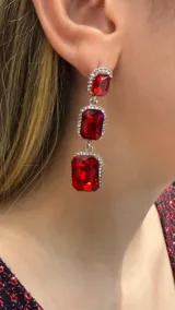 Aros colgantes de diseño articulado con tres cristales rectangulares de color rojo, rodeados por pequeños brillantes plateados.