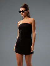 Vestido corto negro strapless, de corte ajustado en el torso con fruncidos laterales y falda levemente evasé.
