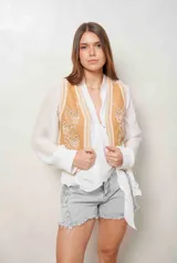 Chaleco de denim color camel con bordados florales en blanco y aplicaciones de perlas en el frente.