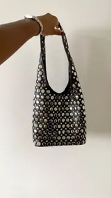 Mini cartera de hombro color negro, totalmente cubierta de tachas metálicas plateadas circulares. Posee un diseño estructurado con asa integrada.