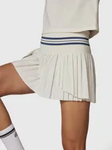 Falda tipo skort con diseño plisado, confeccionada en tejido técnico de secado rápido. Presenta una cintura alta elástica con detalle de rayas horizontales en color azul marino y short integrado con bolsillo.