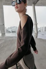 Jersey de punto color marrón oscuro, con cuello redondo y manga larga. Presenta un diseño con aberturas y nudos decorativos en los hombros.