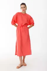 Vestido midi color coral confeccionado en lino. Tiene corte recto, mangas abullonadas con detalle de tablas en el puño, tajos laterales y lazo en la cintura.