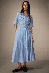 Vestido midi de algodón con estampado de rayas verticales, cuello solapa, manga corta con puños y cierre frontal de botones. Presenta bolsillos con solapa en el pecho y un cinturón de la misma tela para ajustar la cintura.