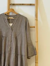 Vestido amplio de lino color verde lima, con cuello mao y abertura frontal con botones de coco. Presenta un diseño con canesú fruncido y volados en los puños de las mangas largas.