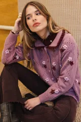 Saco de punto color rosa con bordados artesanales de flores. Presenta un cuello con detalle de volados en color bordó, cierre frontal con botones y diseño de calados en forma de rombos.