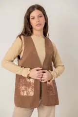 Chaleco de cuero marrón con diseño sin mangas, corte recto y bolsillos frontales con detalle metalizado en tono cobre. Presenta costuras decorativas en los bordes y en los bolsillos.