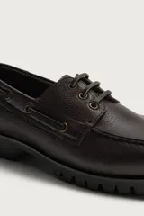 Zapato tipo náutico de piel marrón con acabado abatanado, pas Cordones del mismo tono, ojetes metálicos, plantilla de piel y suela track de goma.