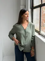 Blusa de color verde oliva con escote en V, cierre frontal con botones y mangas largas con puños elásticos.