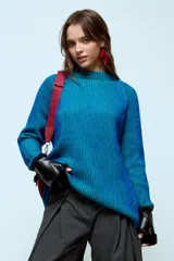 Sweater de punto con hilo de lurex brillante, color azul con rayas verticales en verde. Presenta cuello redondo, mangas largas con puños de piel sintética negra y corte holgado.