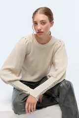 Sweater color crema de tejido de punto con lurex, mangas abullonadas y puños con botones metálicos.