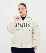 Campera bomber de microfibra color beige con estampado frontal de lettering 'PARIS 1985'. Presenta cierre frontal con cremallera, cuello alto, bolsillos funcionales y puños y ruedo ajustados con elástico.