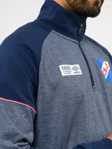 Buzo deportivo de medio cierre marca Umbro del Club Nacional de Football. Presenta un diseño en tonos azul y gris jaspeado, con cuello alto, mangas largas y detalles de costuras en contraste. Incluye el escudo del club y logo de la marca en el pecho.