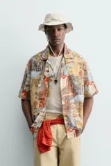 Camisa de corte relajado confeccionada en tejido ligero de algodón, con cuello bowling y manga corta. Presenta un estampado integral con motivos urbanos y tropicales en tonos cálidos.