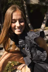 Chaleco de denim azul con estampado paisley, sin mangas, con volados en hombros y cuello, cierre frontal con botones metálicos y bolsillos laterales.